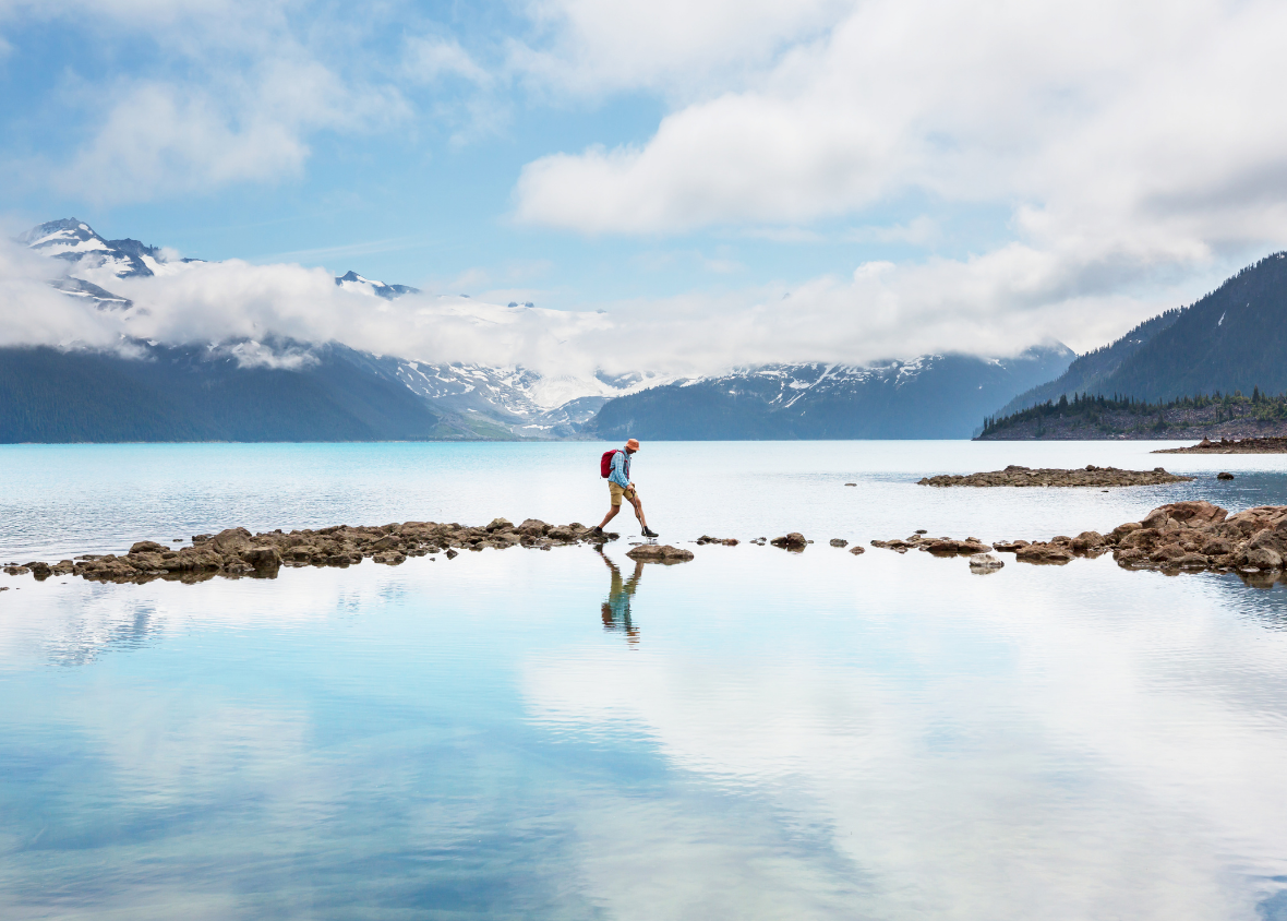 Hiker crossing a lake surrounded by mountains. Like any adventure, the best examples of data discovery are a journey