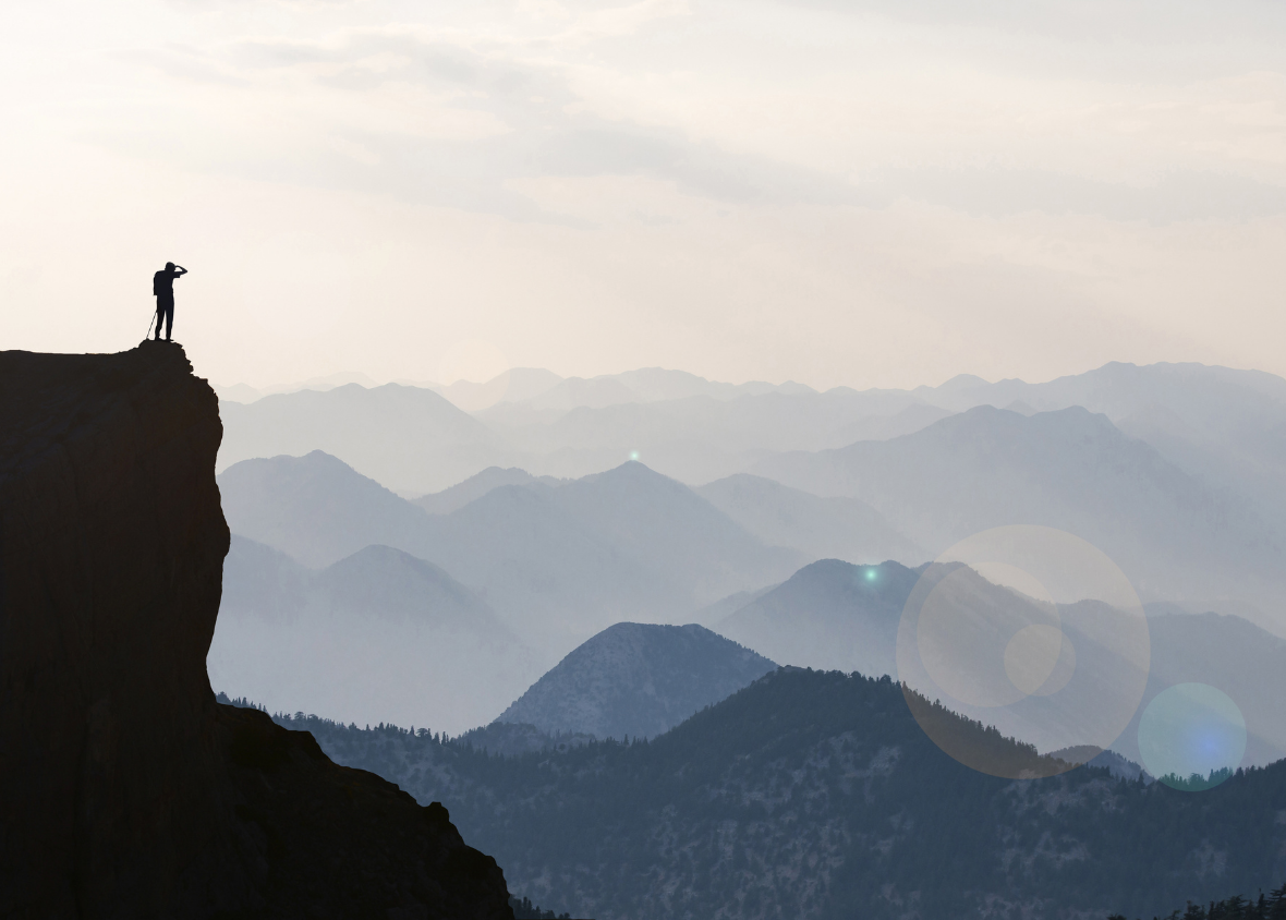 Hiker standing atop a precipice looking out over a wide mountain landscape