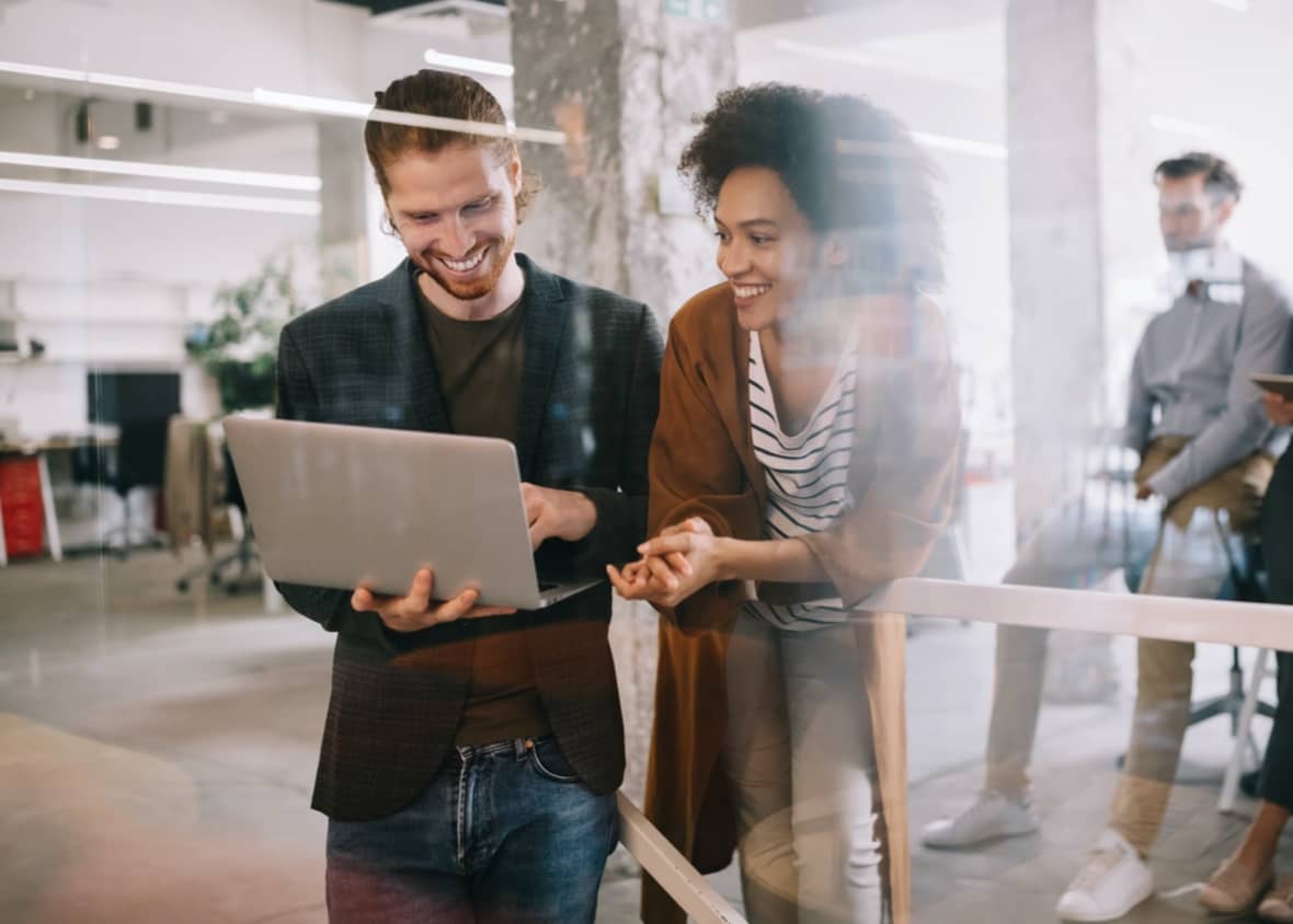 Two smiling young professionals reviewing a data project on a laptop